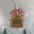 A personalized wooden house-shaped ornament hanging from a red and white striped ribbon. The ornament has a dark green center panel with the text 'THE PATERSON FAMILY' and '300 JAMES AVE' in light wood.