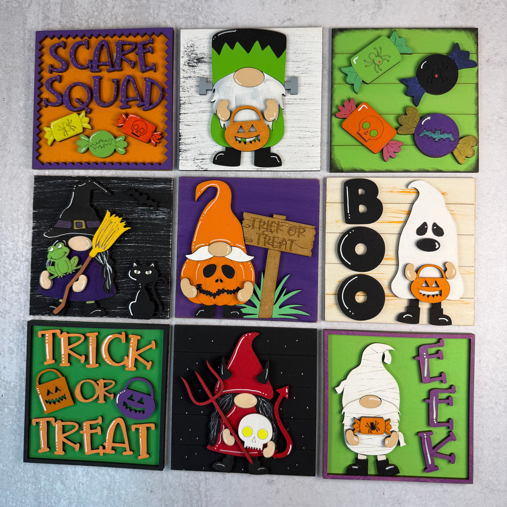 A set of nine square Halloween-themed decorative tiles or signs arranged in a 3x3 grid on a light gray textured background. Each tile features a different spooky design, including pumpkins, ghosts, witches, gnomes, candy, and words like 'Scare Squad,' 'Trick or Treat,' 'Boo,' and 'Eek.