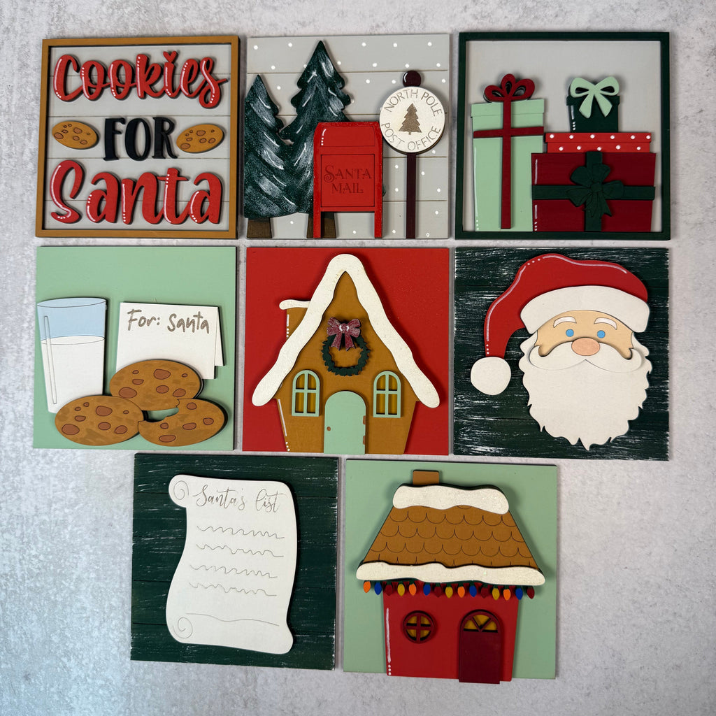 A set of nine square Christmas-themed card or plaque designs arranged on a light gray textured surface. The designs include Santa, cookies, gifts, a house, a Santa list, and holiday motifs in red, green, white, brown, and black.