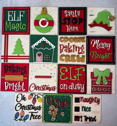 A set of 15 Christmas-themed square ceramic tiles or coasters arranged on a light gray surface. The designs feature festive holiday graphics and text such as 'ELF Magic', 'Santa Stop Here', 'Cookie Baking Crew', 'Merry Bright', 'Elf on Duty', 'Oh Christmas Tree', and 'Naughty Nice I Tried'.
